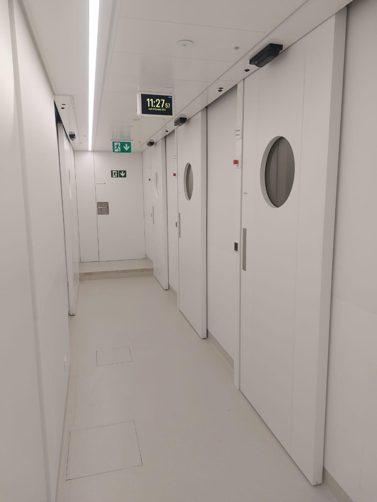 Couloir blanc bordé de portes coulissantes automatiques à hublot